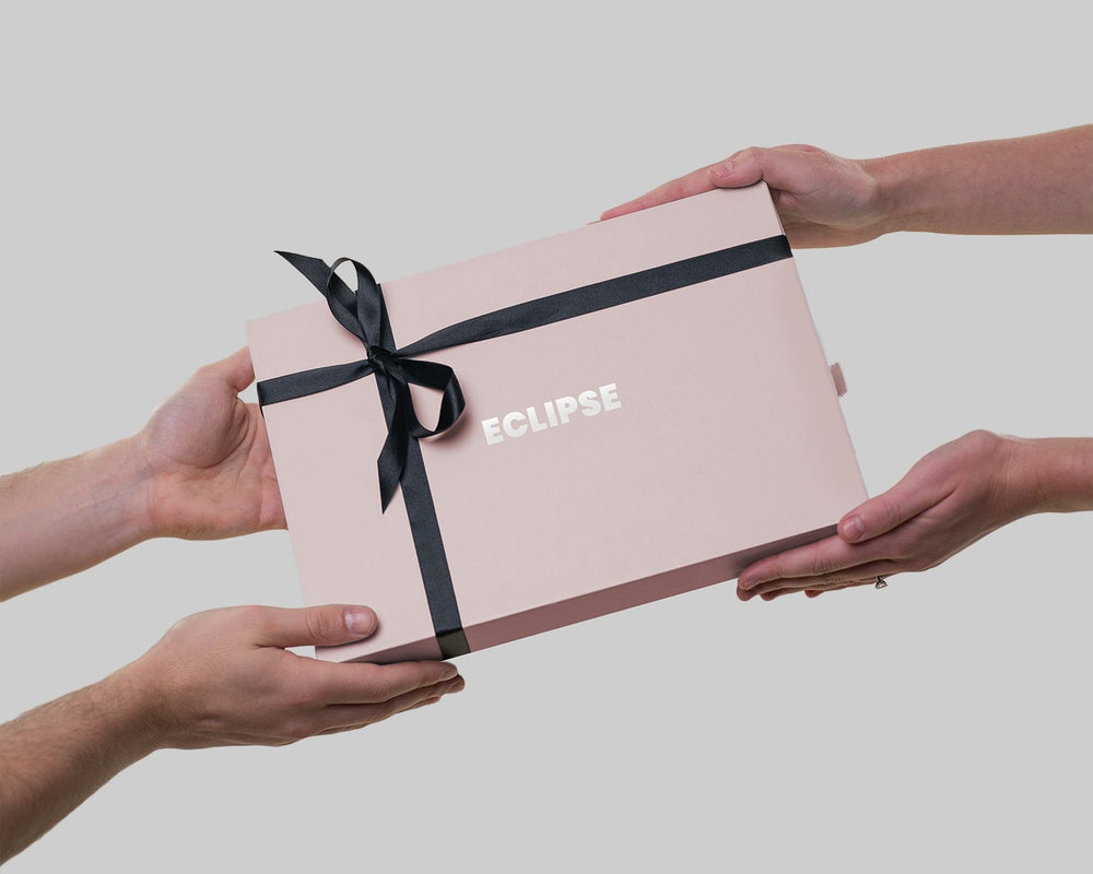 Hands passing a LUNA London ECLIPSE mirror gift box tied with a ribbon