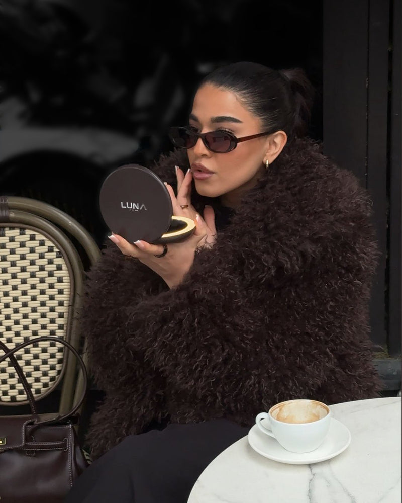 Woman at a café checking her lipstick in an Espresso Brown COMPACT light up compact mirror
