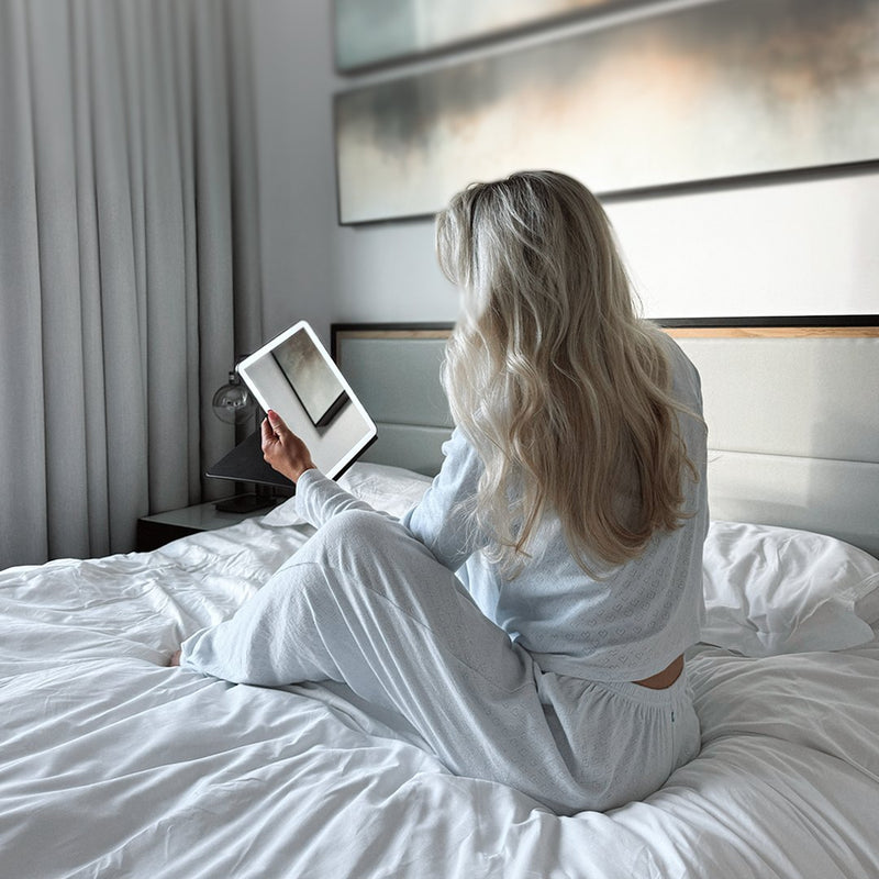 Woman on a hotel bed using an ECLIPSE travel mirror with light